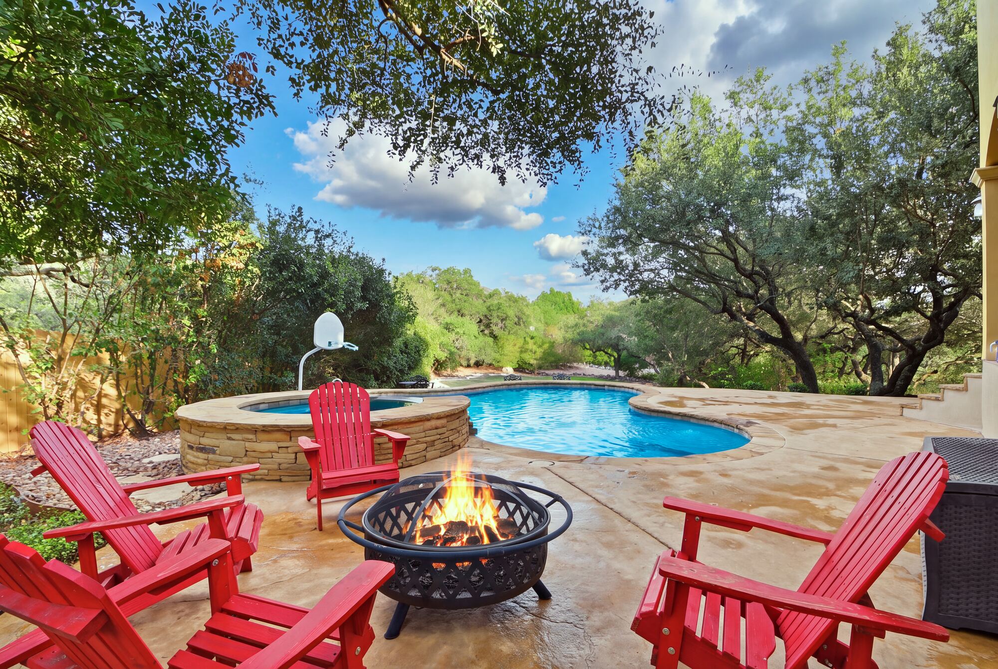 Backyard pool and raised spa on a stone deck, framed by mature trees